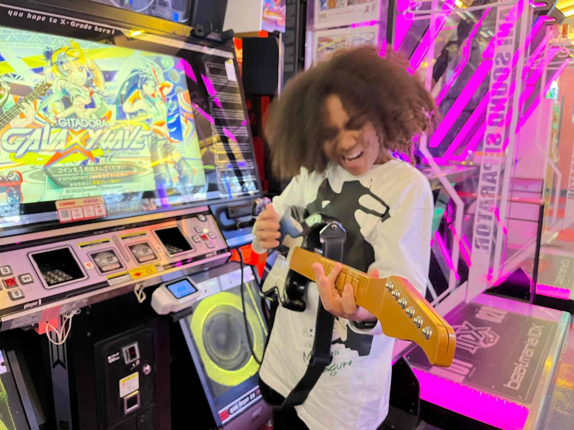 A guest playing the Gitadora rhythm guitar game in Akihabara