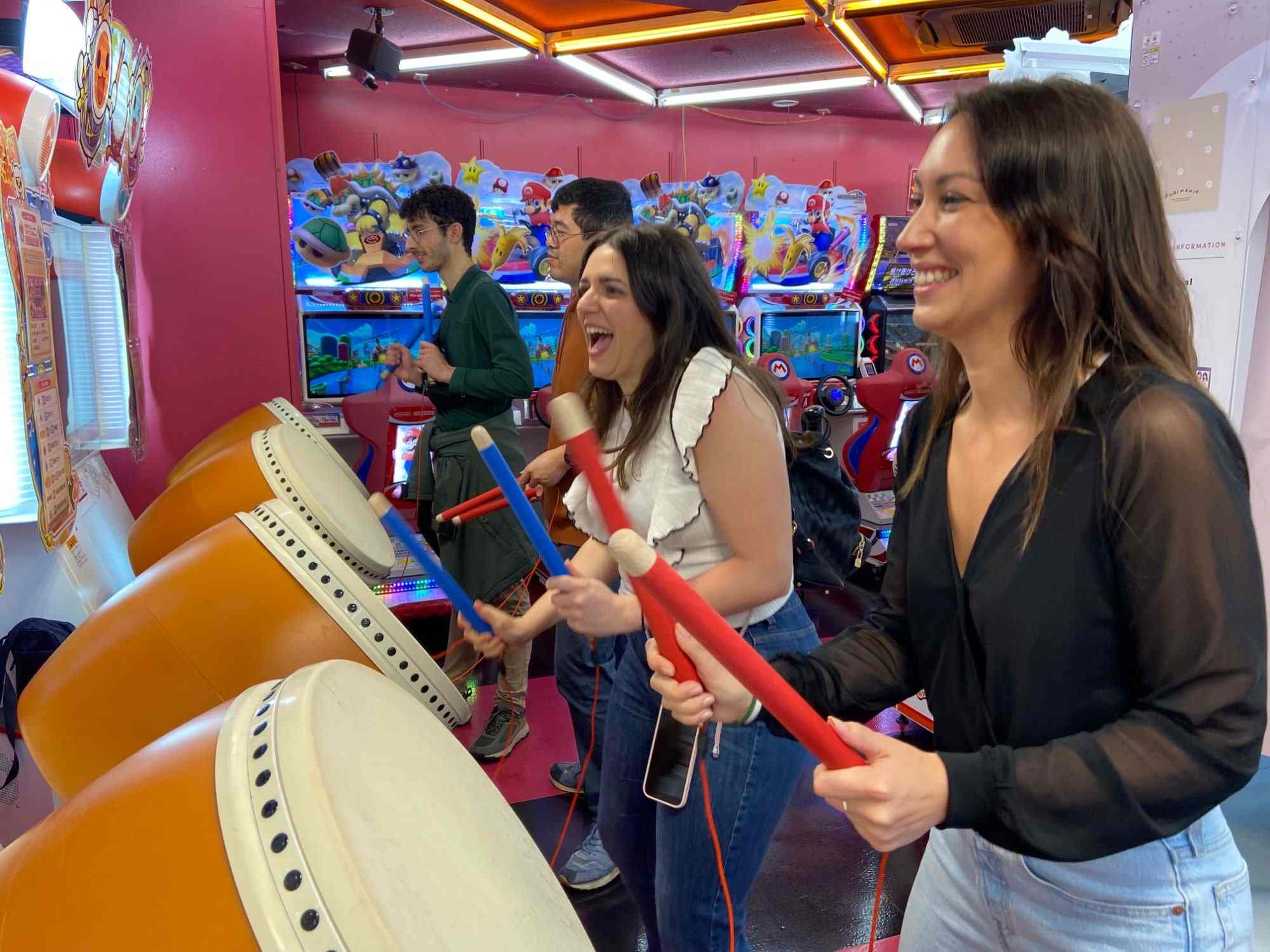 Friends laughing as they play Taiko no Tatsujin drums in a Tokyo arcade