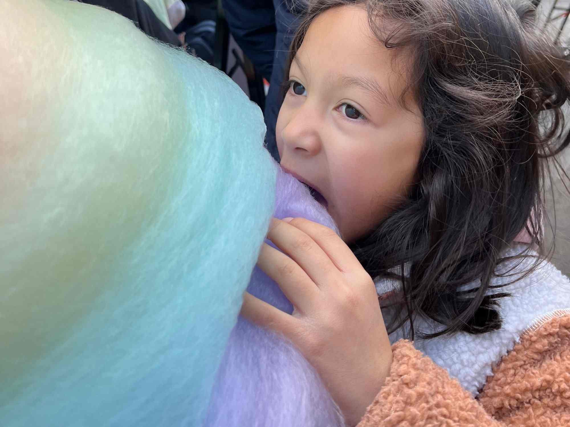 A young girl biting into giant rainbow cotton candy in Harajuku