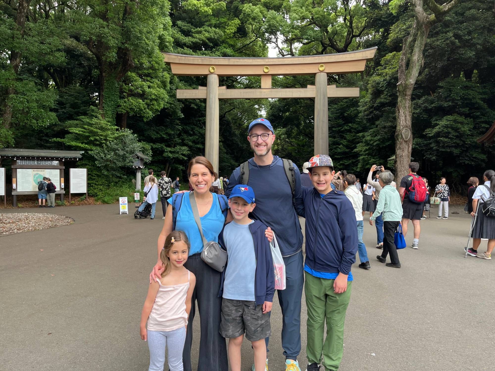 A family of five with three kids smiling in front of the great wooden torii gate at Meiji Jingu