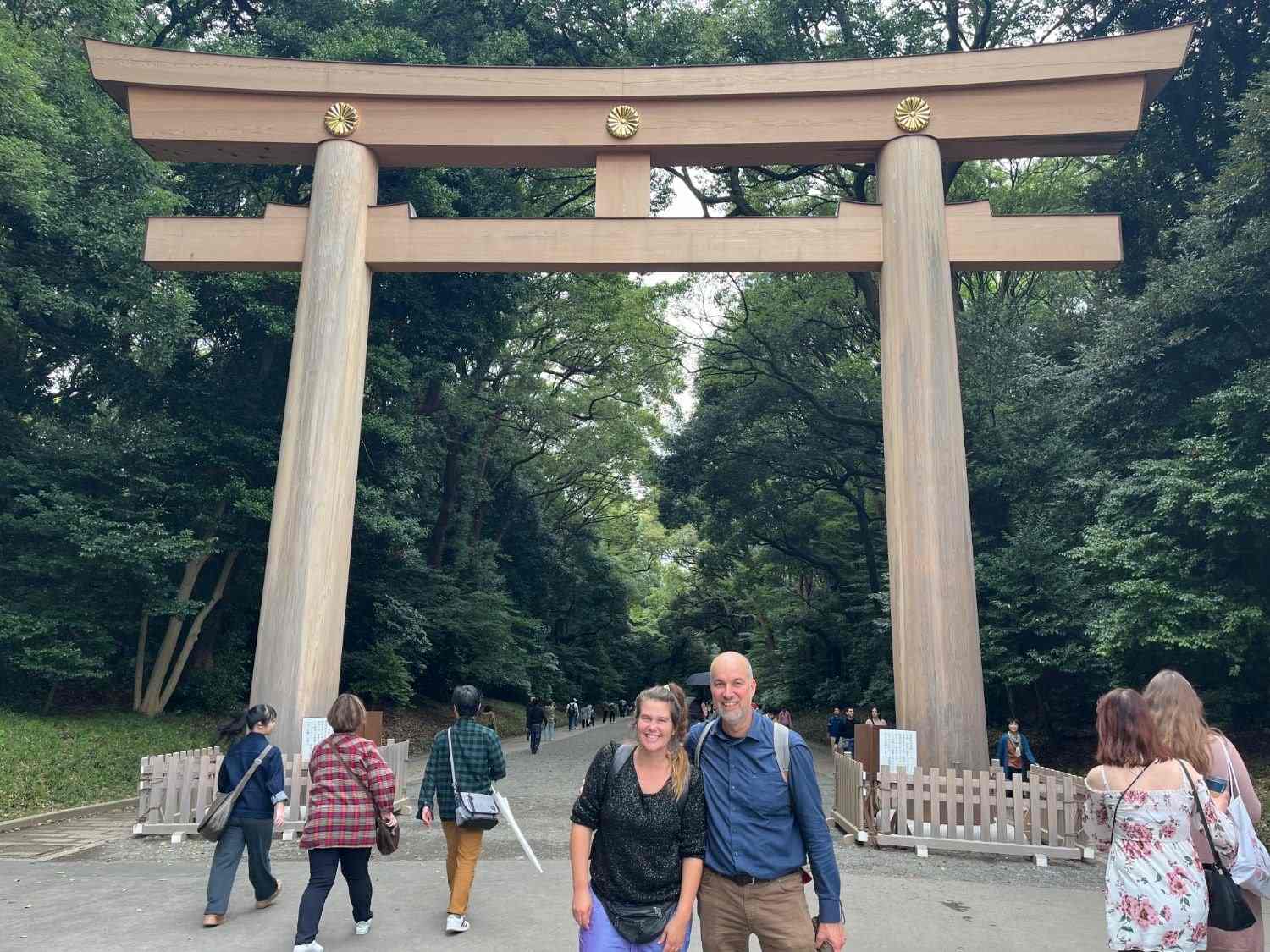 A couple standing on the gravel path below the great wooden torii at Meiji Jingu