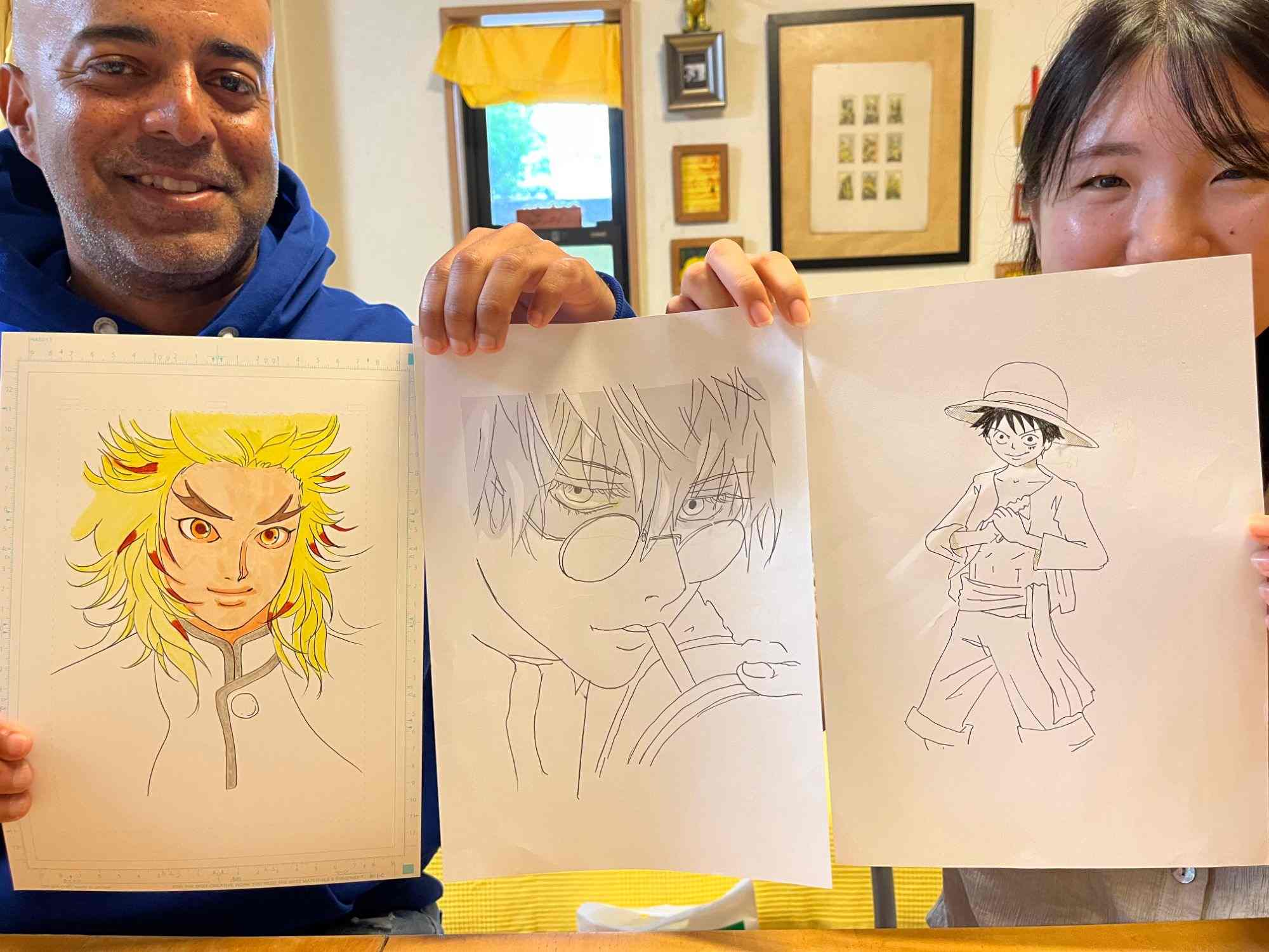 Two participants holding up three finished manga character drawings in the studio