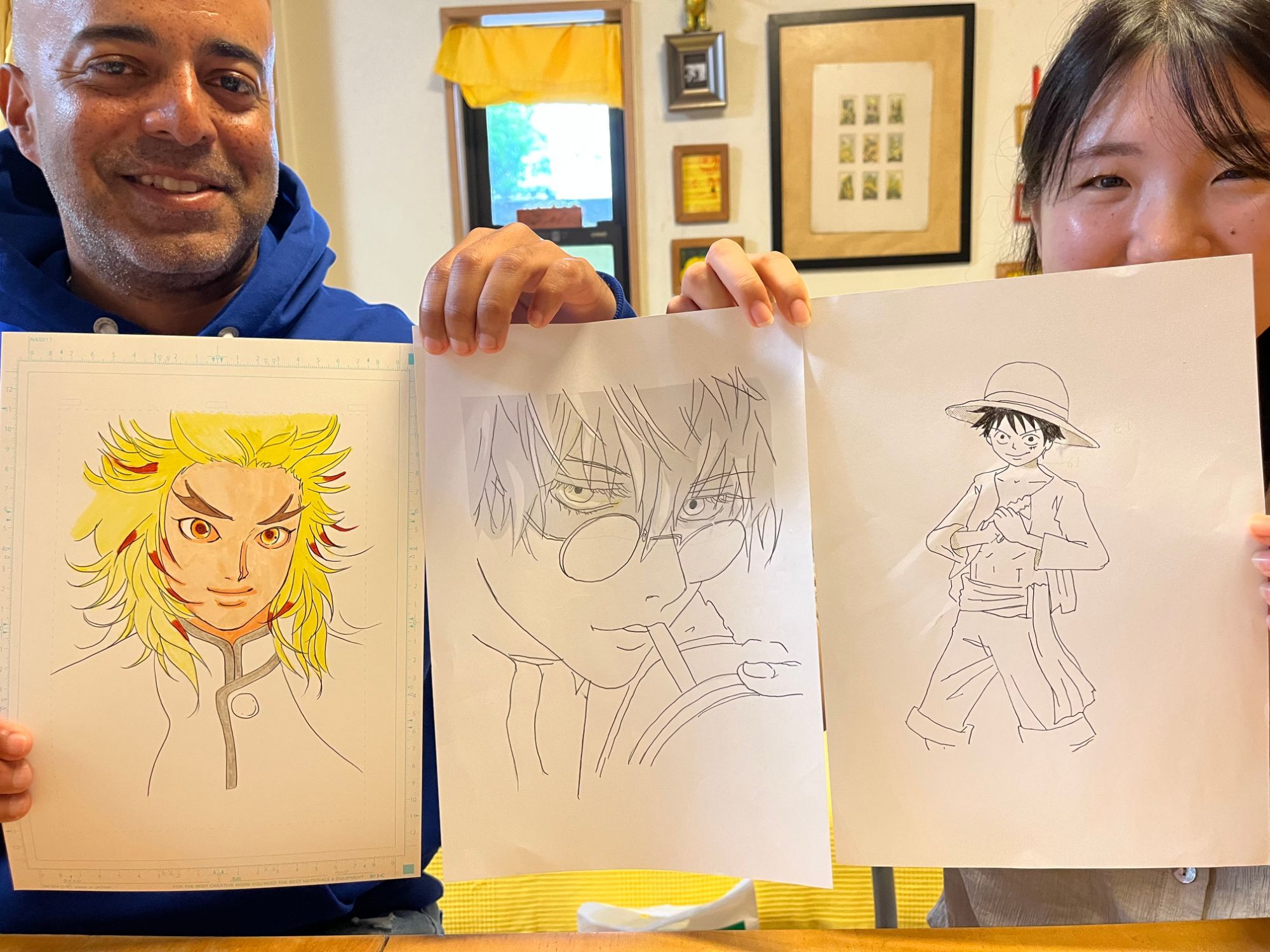 Two participants holding up three finished manga character drawings in the studio